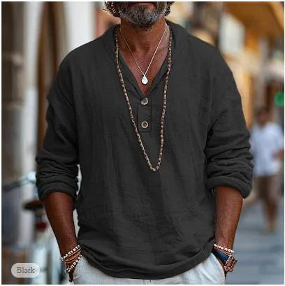 Man in a black linen popover shirt with relaxed V-neck collar, standing outdoors on a cobblestone street.