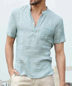 Man wearing a light sky blue linen short sleeve shirt with rolled cuffs and open collar, hand in pocket.
