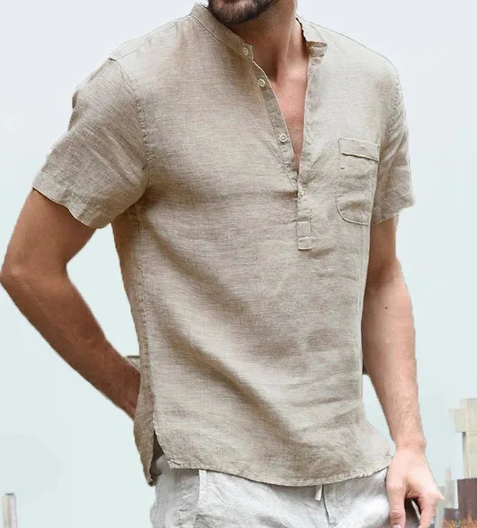 Man wearing a beige linen short sleeve shirt with button placket and chest pocket, hand resting at the waist.