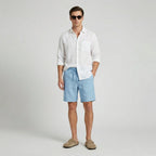 Man wearing light blue linen shorts with a white linen shirt and suede slides, full body front view