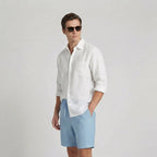 Side profile of a man wearing light blue linen shorts paired with a white linen shirt and sunglasses