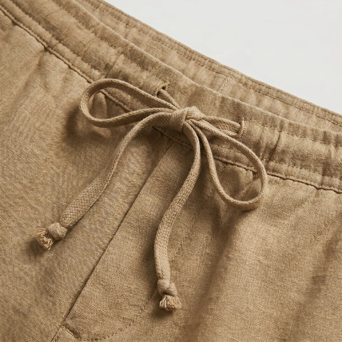 Close-up of the knotted drawstring cord on khaki linen shorts
