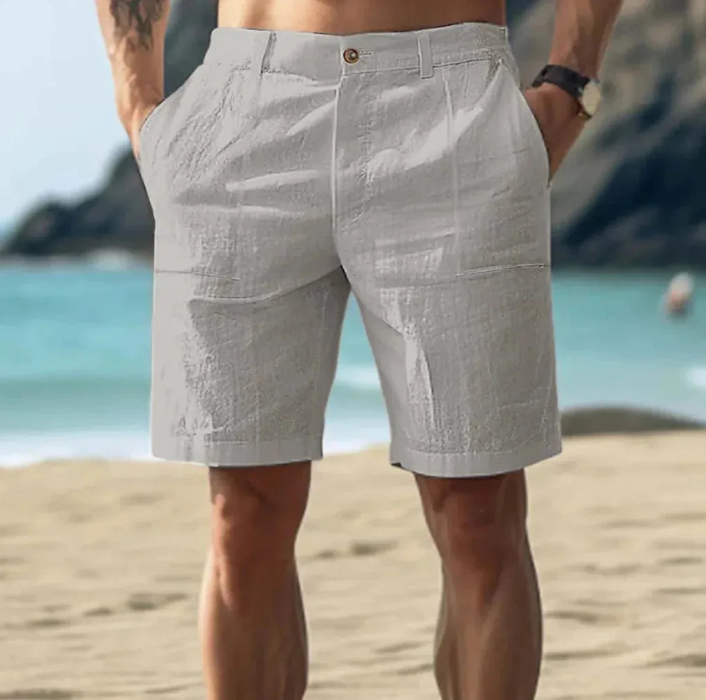 Grey linen-textured shorts seen from behind, highlighting the relaxed fit and side pocket seams on a sandy beach.