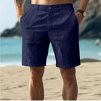 Dark navy linen-textured shorts worn at the beach, rear angle showing the button waistband and tailored leg shape.