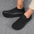 Pair of black knit sneakers worn on feet, standing on grey carpet, matte black sole detail