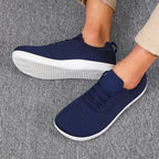 Navy blue knit sneakers worn on feet, white textured sole, lace detail visible at front