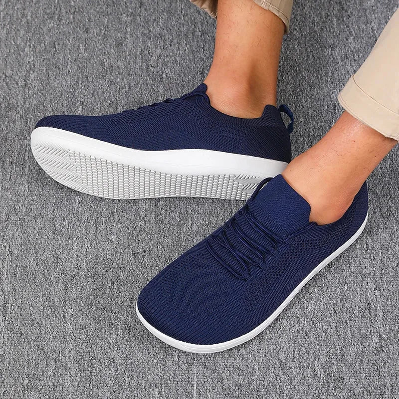 Navy blue knit sneakers worn on feet, white textured sole, lace detail visible at front