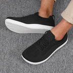 Dark grey knit sneakers on feet, white sole, side angle showing mesh knit pattern