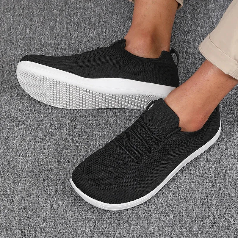 Dark grey knit sneakers on feet, white sole, side angle showing mesh knit pattern