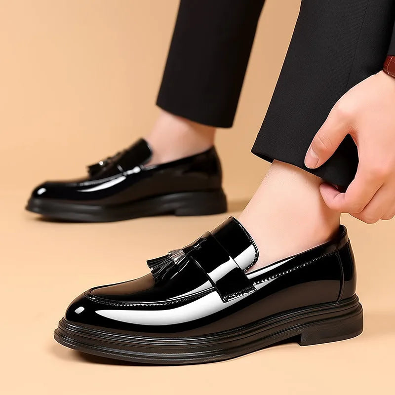 Side profile of a glossy black patent leather tasselled loafer with chunky ribbed platform sole, worn with tailored black trousers.