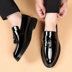 Overhead view of a matching pair of patent leather tasselled loafers on bare feet, showing the rounded toe and glossy finish.
