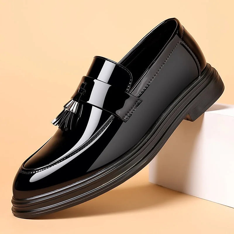 Close angled shot of a single loafer resting against a white block, highlighting the mirror-shine patent finish and tassel trim.