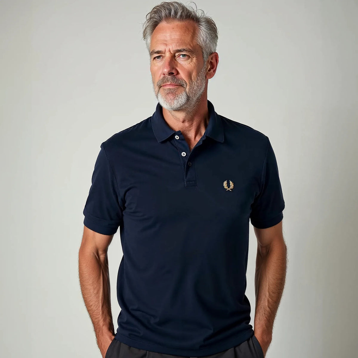 Older man wearing a navy pique polo shirt with gold laurel wreath emblem and classic point collar