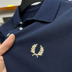 Close-up of navy pique fabric with tan laurel wreath embroidery and silver-tone buttons on the collar placket