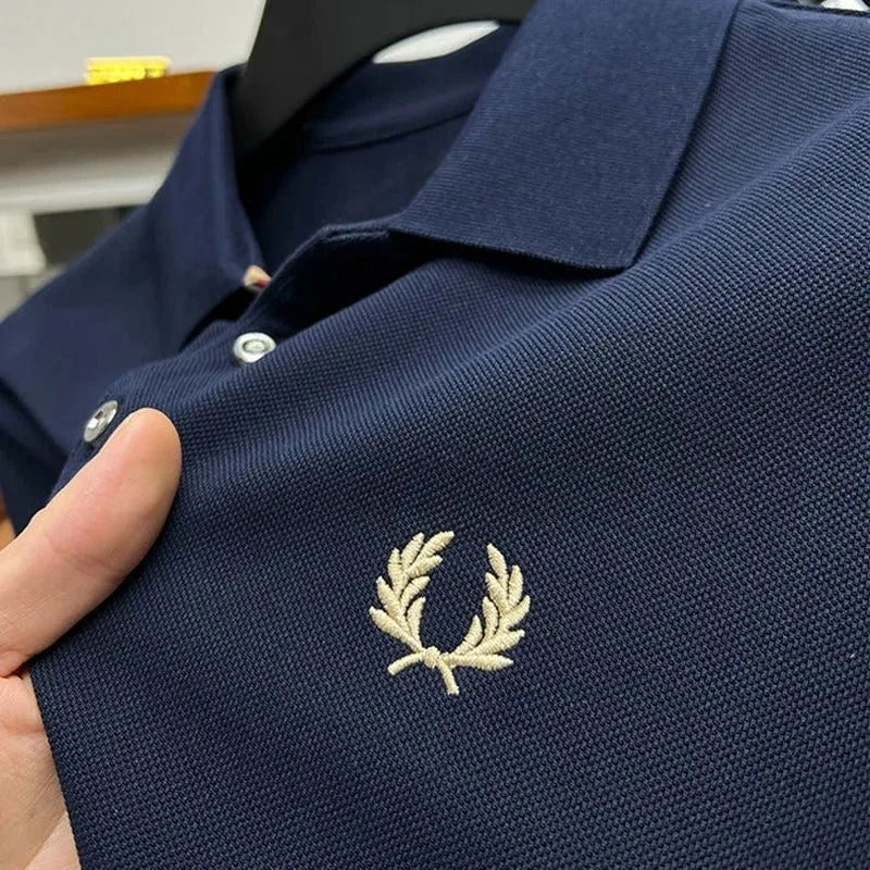 Close-up of navy pique fabric with tan laurel wreath embroidery and silver-tone buttons on the collar placket