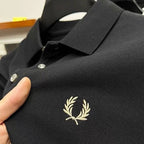 Close-up of black pique polo fabric showing cream laurel wreath embroidery and the ribbed collar