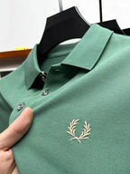 Close-up of sage green pique polo with cream laurel wreath embroidery and matching collar