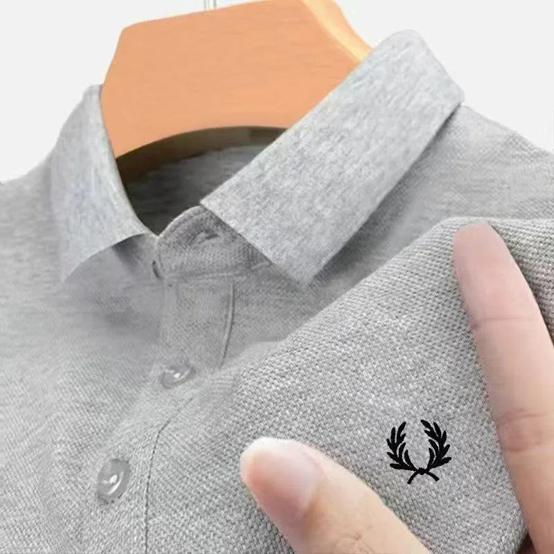 Close-up of light grey marl polo fabric with black laurel wreath embroidery, finger pointing at the logo