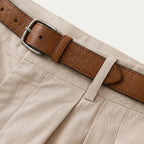 Close-up of the tan leather belt and buckle on the waistband of the beige pleated chino shorts