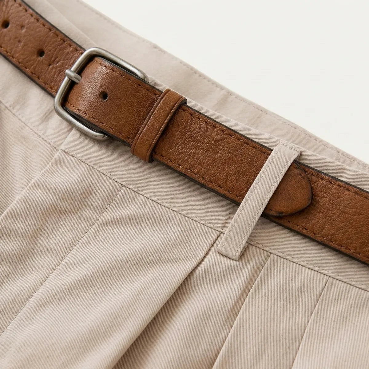 Close-up of the tan leather belt and buckle on the waistband of the beige pleated chino shorts
