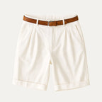 Flat lay of cream pleated chino shorts with turn-up cuffs and a brown leather belt attached