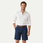 Man wearing a white linen shirt paired with navy pleated chino shorts and a brown leather belt