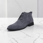 Grey suede chukka boot with lace-up front and black rubber sole, shown at an angle on marble surface.