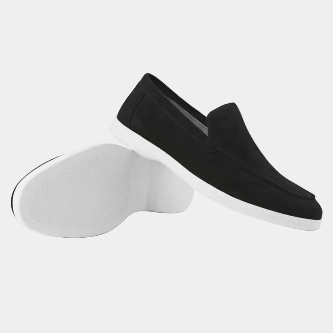 Pair of grey suede loafers arranged together, one upright and one resting on its white sole