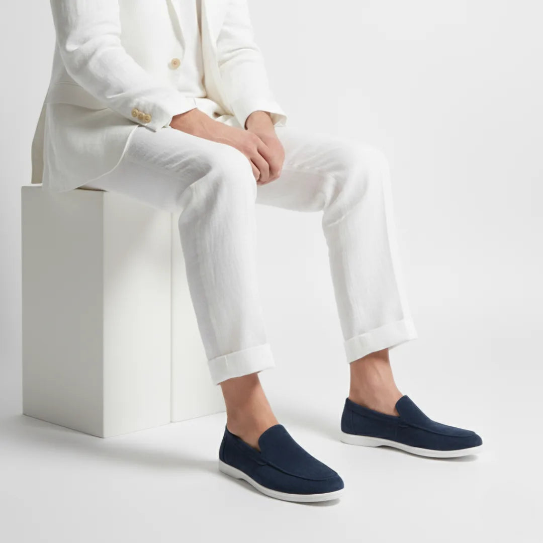 Model seated in a white linen suit wearing navy suede loafers with white soles, styled with cuffed trousers