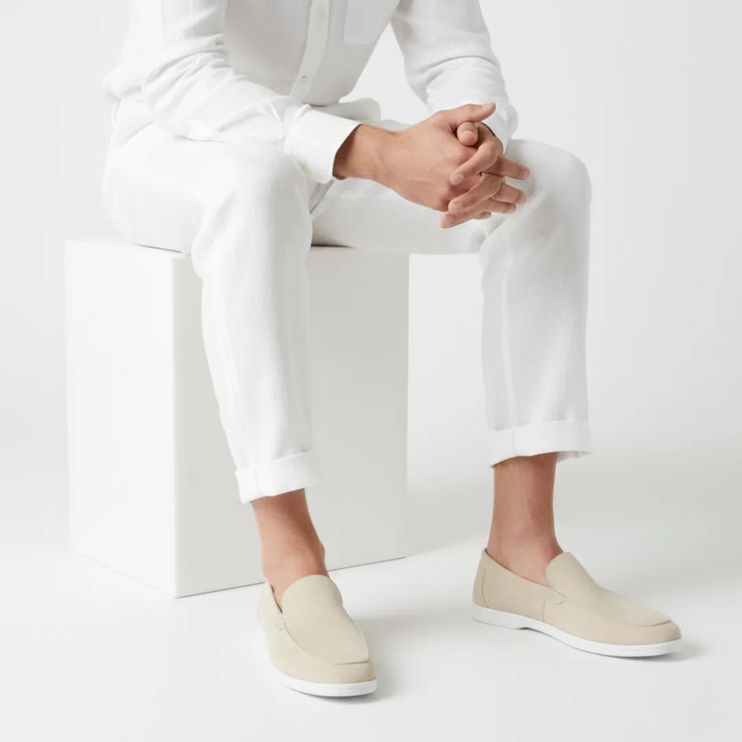 Model seated in white linen separates wearing beige suede loafers with white soles and bare ankles