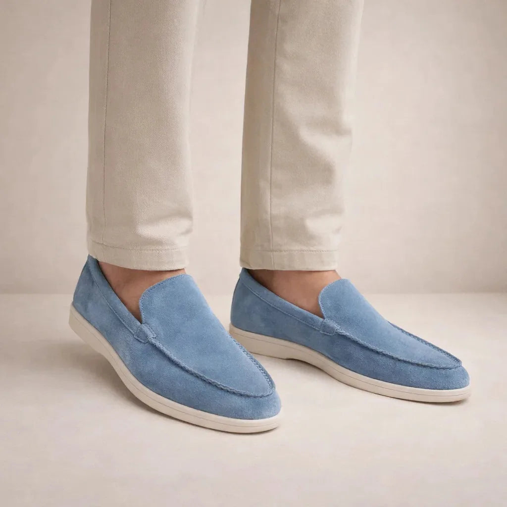 Side view of model wearing light blue suede slip-on loafers with white sole and tan pants