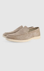 Angled side view of beige suede slip-on loafers with a cream rubber sole on a plain background