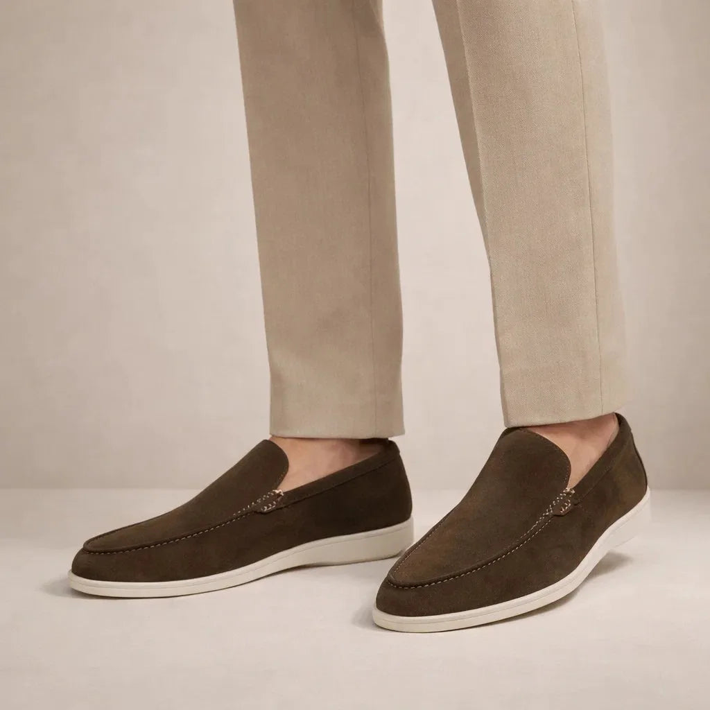 Model wearing dark brown suede loafers with white sole, paired with light beige tailored trousers