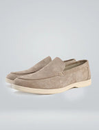 Three-quarter studio shot of beige suede loafers highlighting the apron-toe stitching and sole
