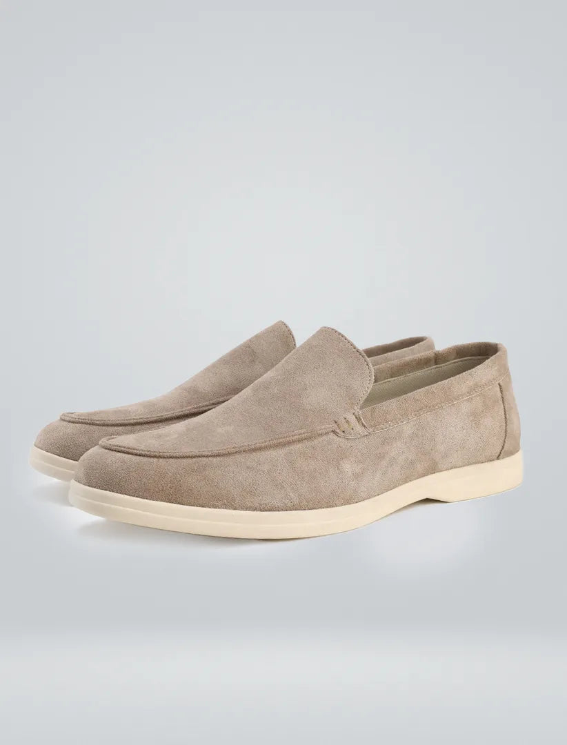 Three-quarter studio shot of beige suede loafers highlighting the apron-toe stitching and sole