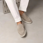 Close-up of beige suede loafers worn with rolled white trousers while seated, feet crossed
