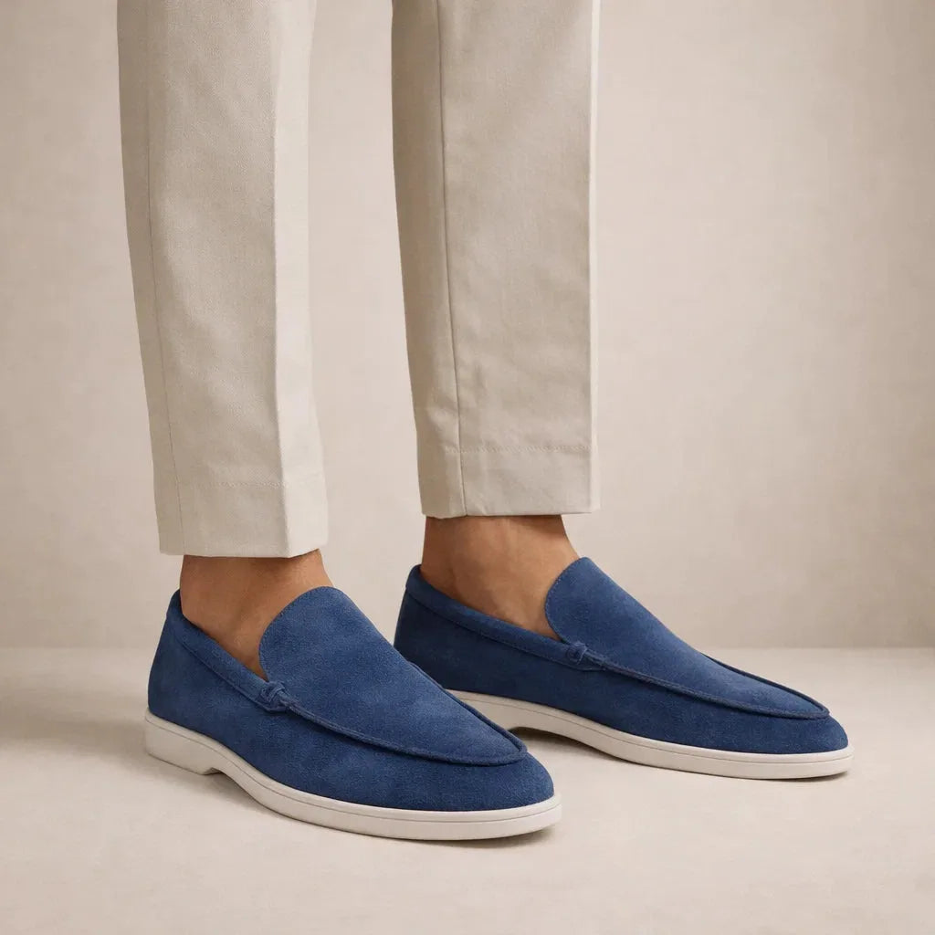 Side view of model wearing navy blue suede loafers with white sole and cream trousers
