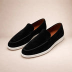 Pair of black suede loafers with white sole shown at an angle on neutral background