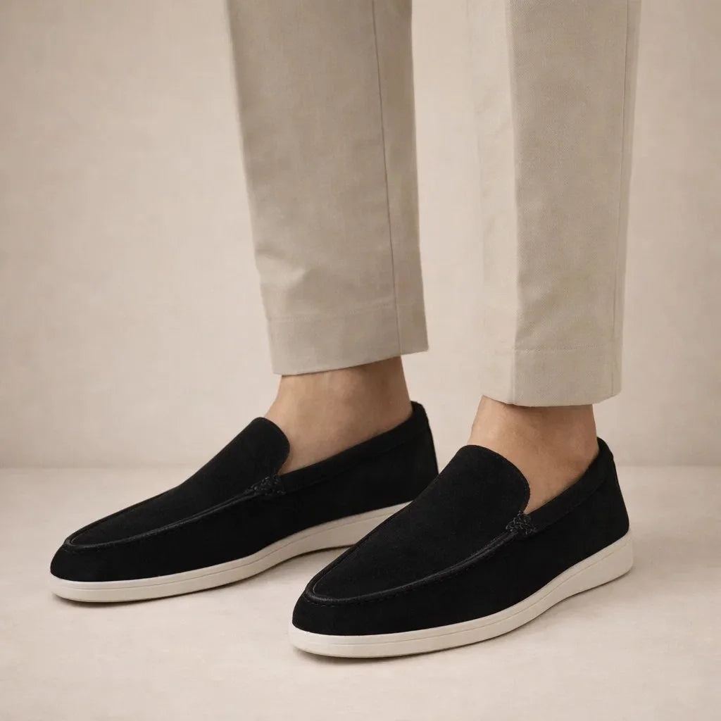 Side view of model wearing black suede loafers with white sole and beige trousers