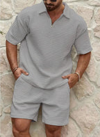 Front view of a man wearing a grey textured polo shirt and matching shorts with a quarter-zip collar, hands in pockets