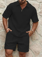 Man wearing a black textured two-piece short sleeve polo and shorts set standing against a stone wall