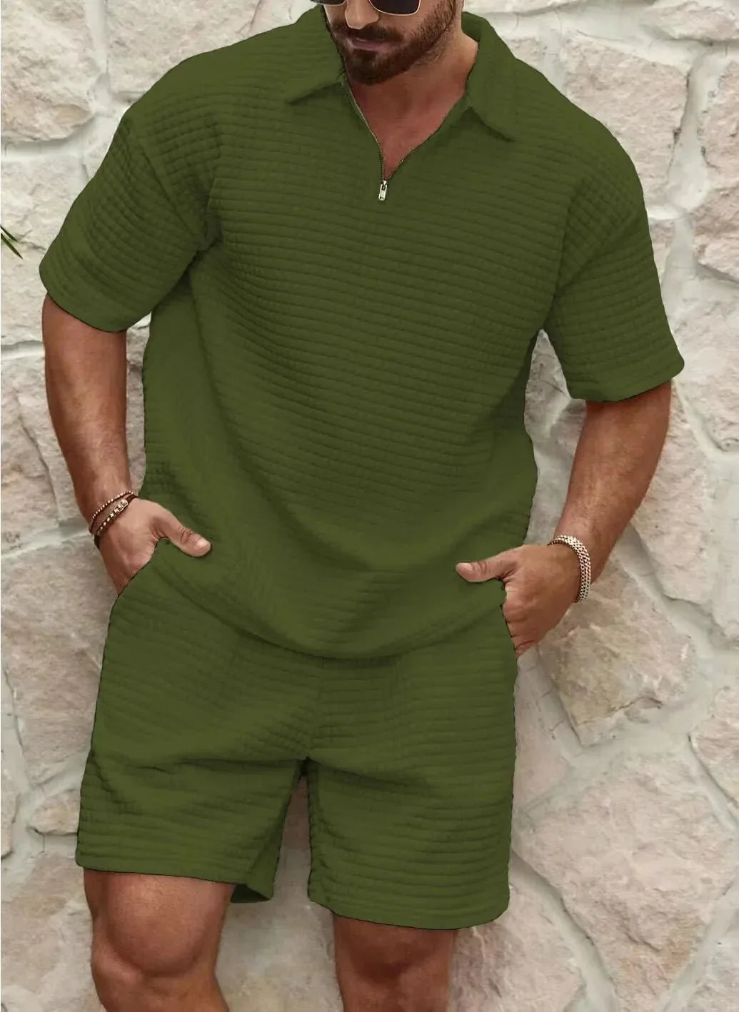 Man wearing an olive green textured polo and shorts set standing against a rustic stone backdrop