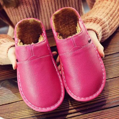 Pink leather slipper pair with contrast stitching and warm fleece lining, cupped in two hands.
