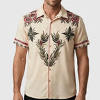Front view of a man wearing a cream short-sleeve shirt with embroidered floral and leaf motifs across the chest and shoulders