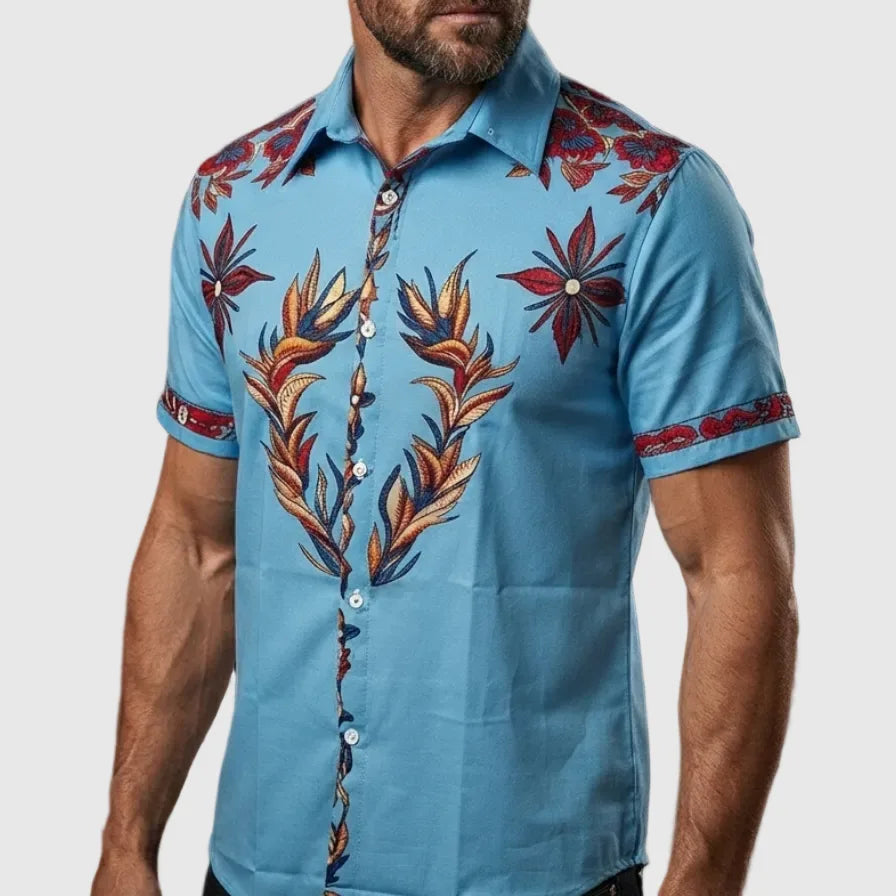 Side view of a man wearing a blue short-sleeve shirt with red and gold leaf and star embroidery on the chest and cuff