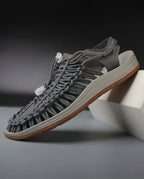 Grey woven cord sandal with tan rubber sole and bungee toggle lacing, angled side view on a grey backdrop