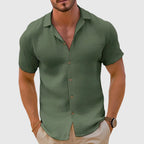Olive green woven short sleeve button shirt with camp collar, paired with beige trousers