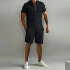 Man wearing a black zip-collar polo shirt and matching tailored shorts with white sneakers, front view