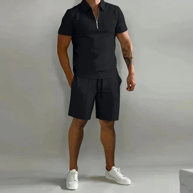 Man wearing a black zip-collar polo shirt and matching tailored shorts with white sneakers, front view