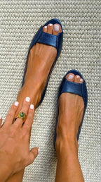 Overhead shot of navy metallic leather peep-toe flats worn on bare feet on a woven rug.